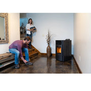 Person using a pellet stove in a home setting with another person on stairs.