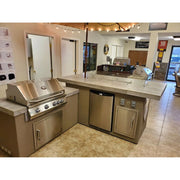 Kokomo Grills Baja/Fire L-Shaped BBQ Island with 4 burner stainless steel grill, outdoor refrigerator, and beige porcelain countertop.