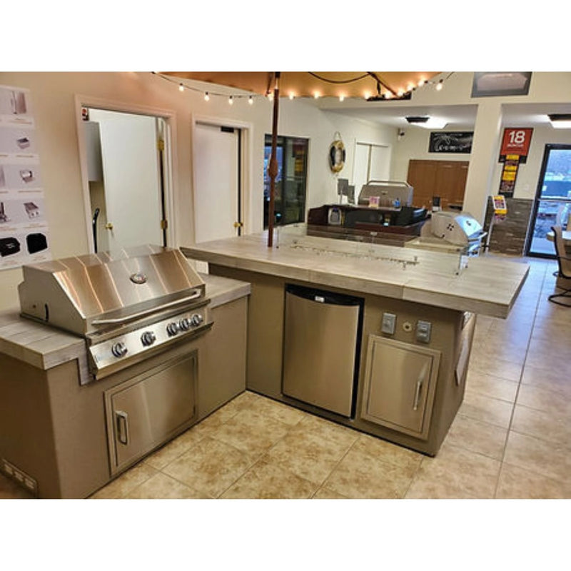 Kokomo Grills Baja/Fire L-Shaped BBQ Island with 4 burner stainless steel grill, outdoor refrigerator, and beige porcelain countertop.