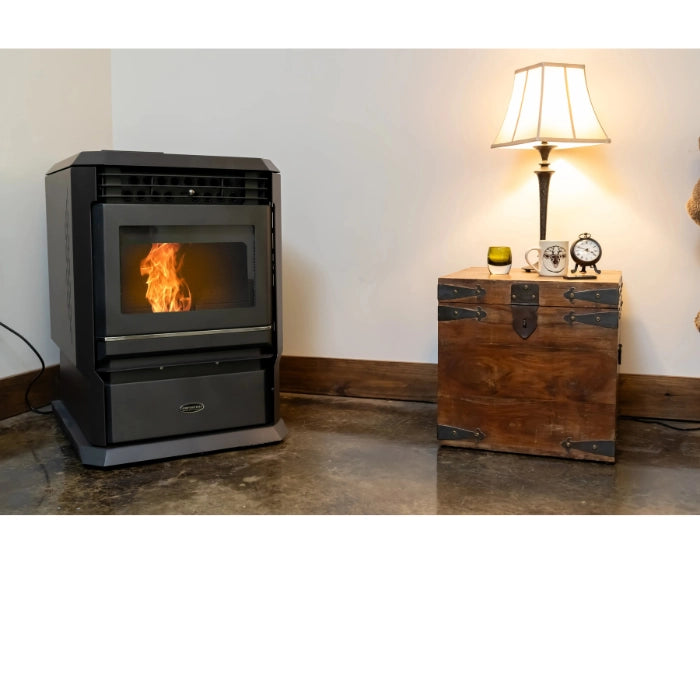 Pellet stove with flames inside, next to a wooden chest and lamp in a room.
