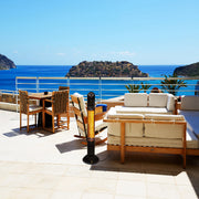 Outdoor patio set with wooden furniture and cushions overlooking a scenic ocean view.
