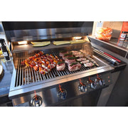 Kokomo Grills Outdoor Kitchen Montego Model BBQ Island with built-in stainless steel grill, control knobs, and integrated lights cooking skewers and steaks.