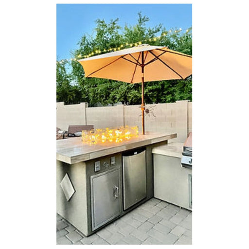 Kokomo Grills Baja/Fire L-Shaped BBQ Island with fire pit, 4 burner grill, outdoor refrigerator, and beige umbrella.