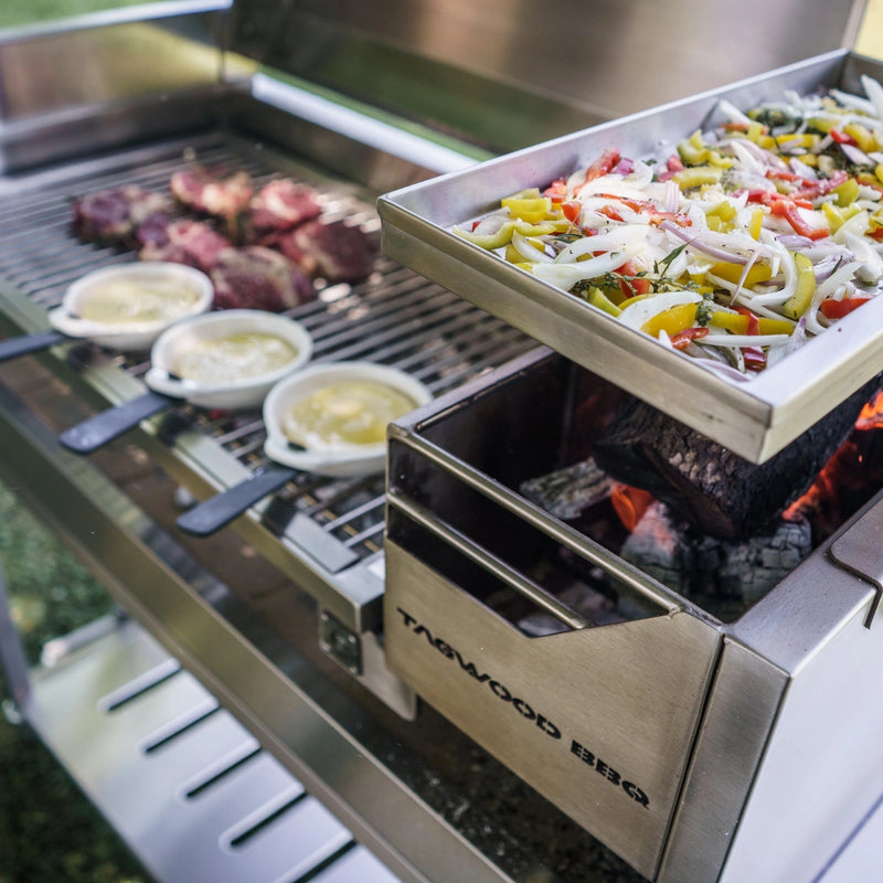 Tagwood BBQ Freestanding Argentine Santa Maria Grill with stainless steel construction, adjustable grates, and gaucho firebox cooking vegetables and meat