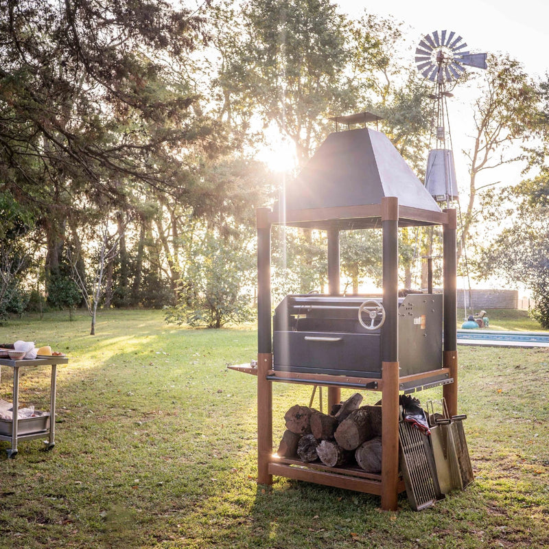 Tagwood BBQ The Beast Argentine Santa Maria Style black steel grill with wood fire brasero and large cooking space outdoors.