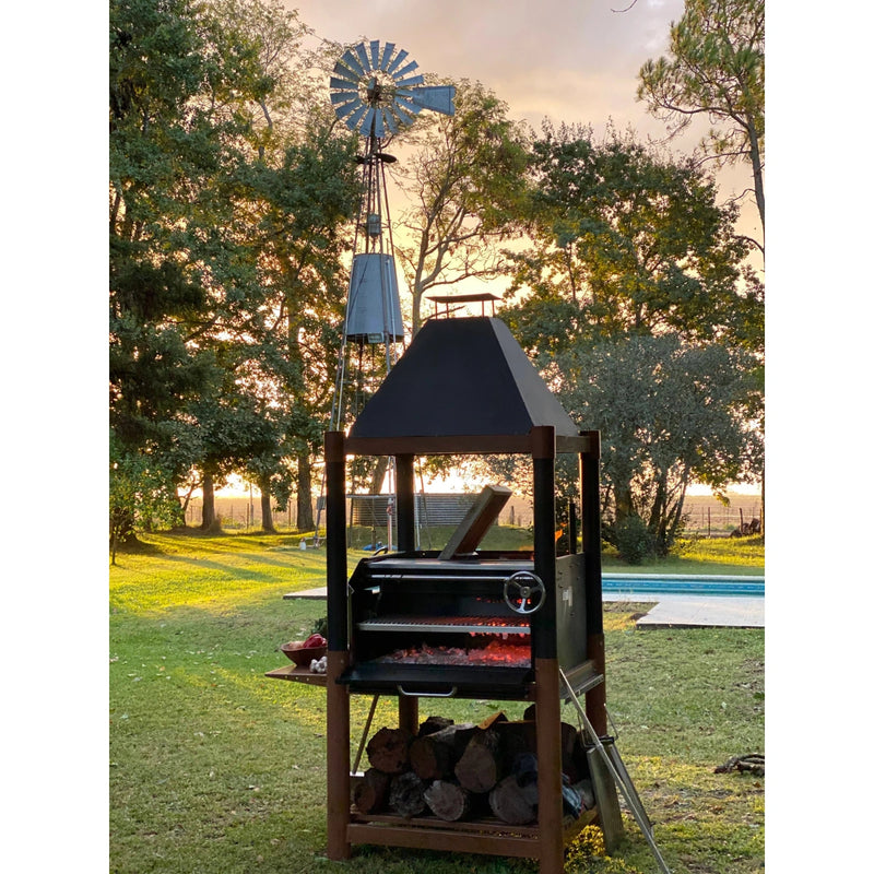 Tagwood BBQ The Beast Argentine Santa Maria Style freestanding black steel grill with peaked roof and wood firebrasero.