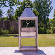 Tagwood BBQ The Beast Santa Maria wood fire grill in stainless steel with peaked roof, height-adjustable grates, and gaucho brasero firebox.