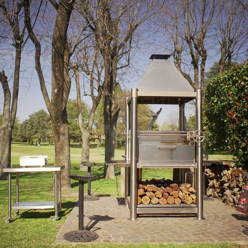 Tagwood BBQ The Beast Santa Maria Wood Fire & Charcoal Grill with 304 stainless steel, adjustable grates, peaked roof, and firewood storage.