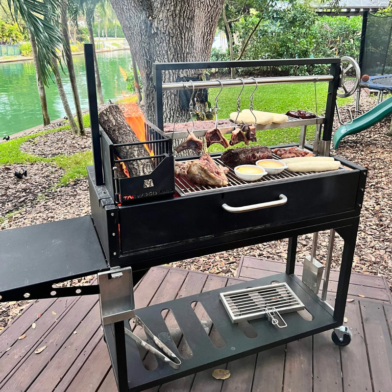 Tagwood BBQ Freestanding Argentine Santa Maria Grill in black steel with hinged grilling grates, brasero firebox, and side shelf outdoors.