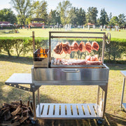 Tagwood BBQ Freestanding Argentine Santa Maria Wood Fire & Charcoal Grill in stainless steel with adjustable grates and gaucho-style firebox outdoors.