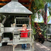 Tagwood BBQ Freestanding Mini Argentine Santa Maria Grill with stainless steel, adjustable grates, gaucho brasero firebox, and peaked roof.