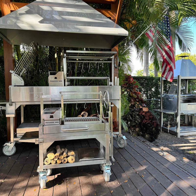 Tagwood BBQ Freestanding Mini Argentine Santa Maria Wood Fire & Charcoal Grill with stainless steel construction, peaked roof, and adjustable grates.