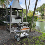 Tagwood BBQ Freestanding Mini Argentine Santa Maria Grill with stainless steel, peaked roof, adjustable grates, and charcoal firebox.