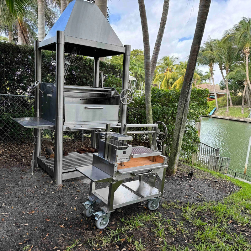 Tagwood BBQ Freestanding Mini Argentine Santa Maria Grill with stainless steel, peaked roof, adjustable grates, and charcoal firebox.