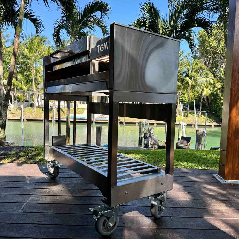 Tagwood BBQ Freestanding Argentine Wood Fire & Charcoal Gaucho Grill BBQ18SS with stainless steel, large cooking area, and wheeled base.