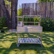 Tagwood BBQ XL Freestanding Argentine Santa Maria Grill with stainless steel, height-adjustable grates, brasero firebox, and side shelf on wheels.