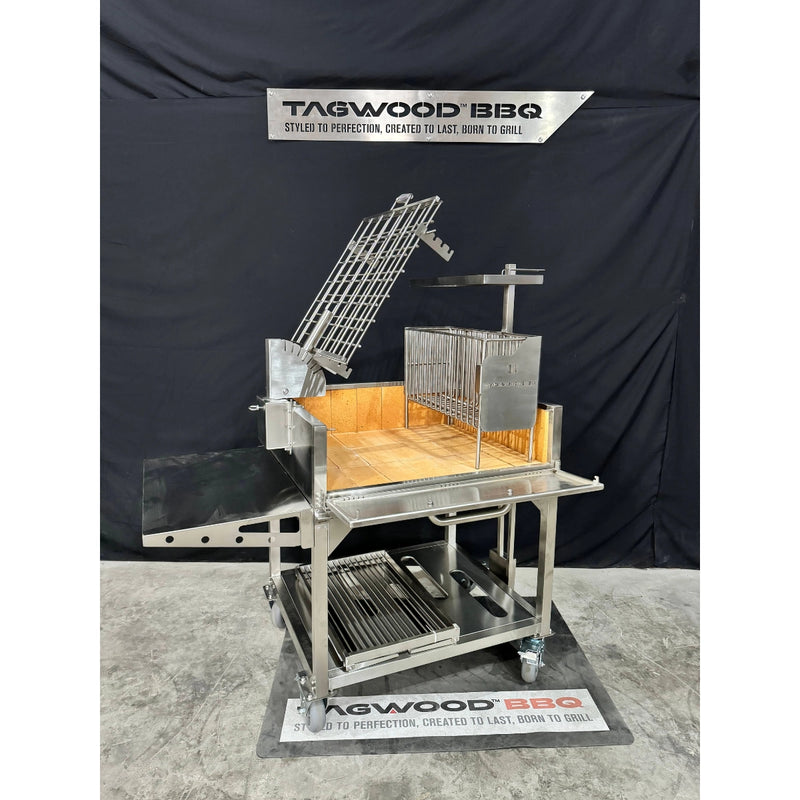 Tagwood BBQ Freestanding Argentine Charcoal Gaucho Grill BBQ33SS with stainless steel clamp grill, firebox, and adjustable grates on casters.