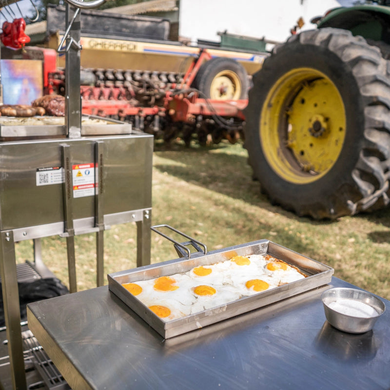 Tagwood BBQ Height Adjustable Griddle - BBQ54SS in stainless steel with adjustable height cooking surface frying eggs outdoors.