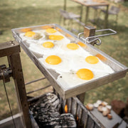Tagwood BBQ Height Adjustable Griddle GRD86SS with stainless steel surface cooking multiple eggs outdoors over charcoal grill