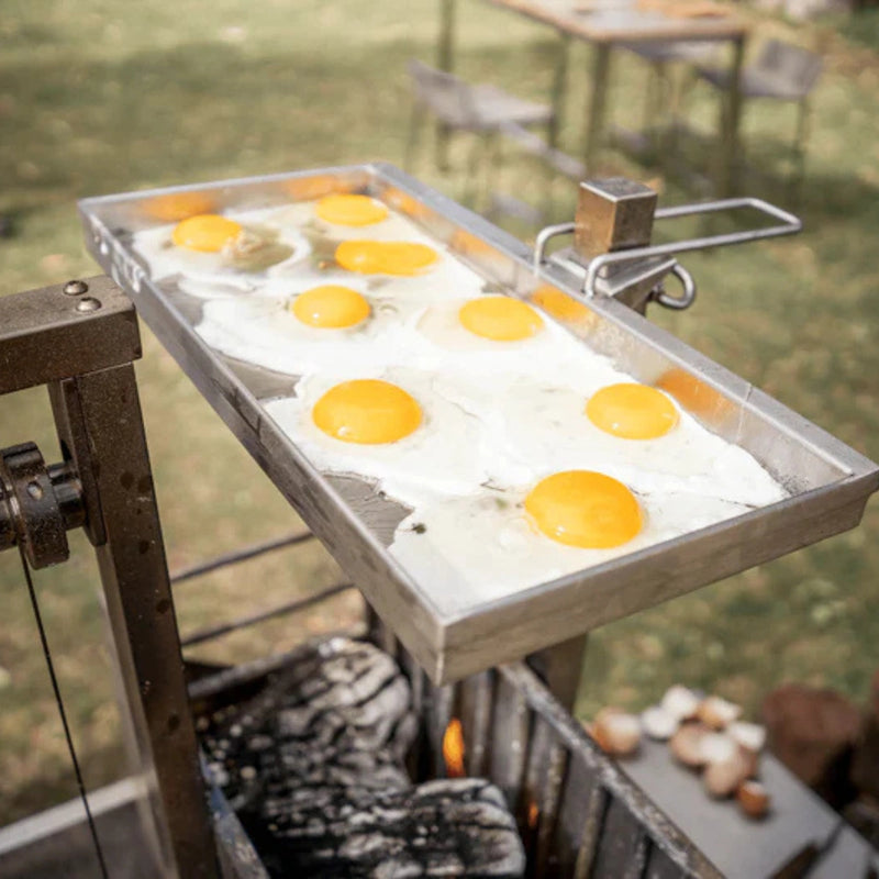 Tagwood BBQ Height Adjustable Griddle GRD86SS with stainless steel surface cooking multiple eggs outdoors over charcoal grill