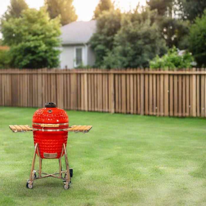 Red barbecue grill on a grassy lawn with a wooden fence and trees in the background