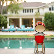 Red barbecue grill on a stand by a pool with a house in the background