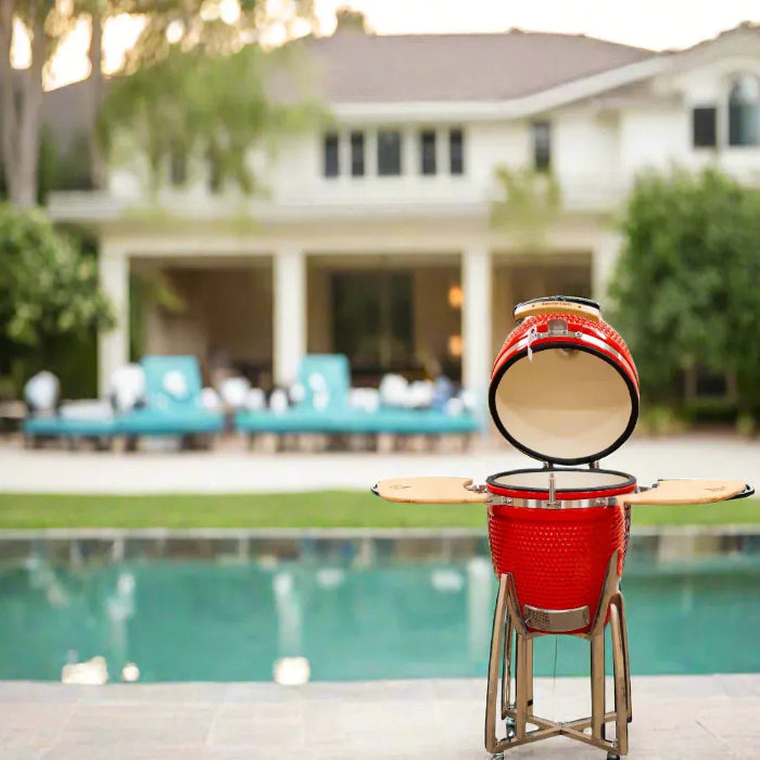 Red barbecue grill on a stand by a pool with a house in the background