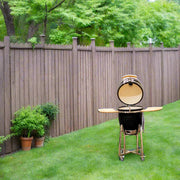 Barbecue grill on a grassy lawn with a wooden fence and trees in the background