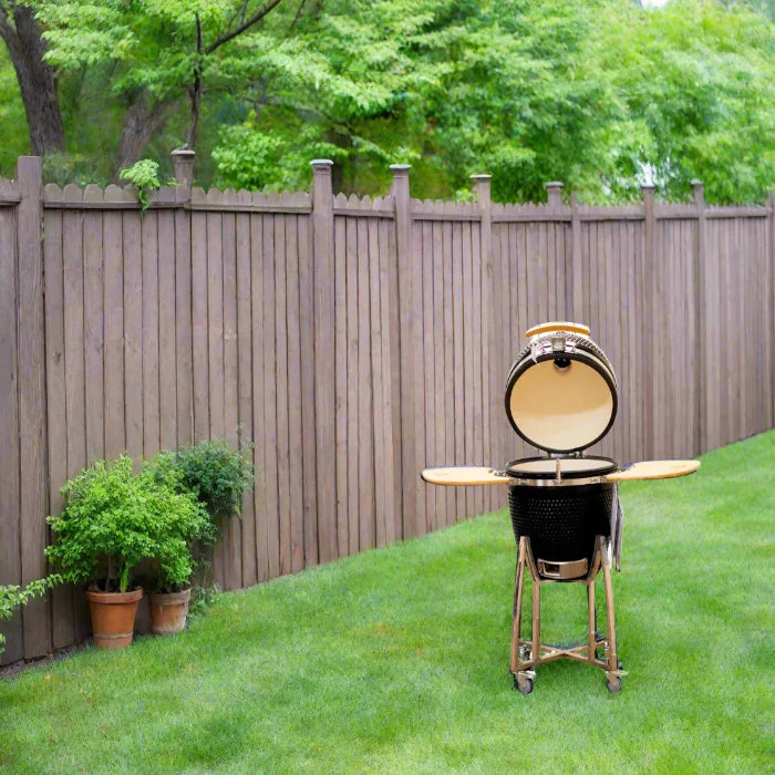 Barbecue grill on a grassy lawn with a wooden fence and trees in the background