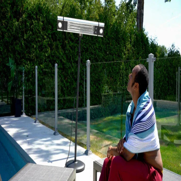 Person sitting on a chair with a towel over their shoulders, looking up at a solar panel system in a garden.