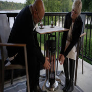 Two people using a patio heater on a deck with a scenic background