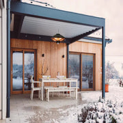 Patio area with a wooden table and chairs in front of a modern house with large windows.