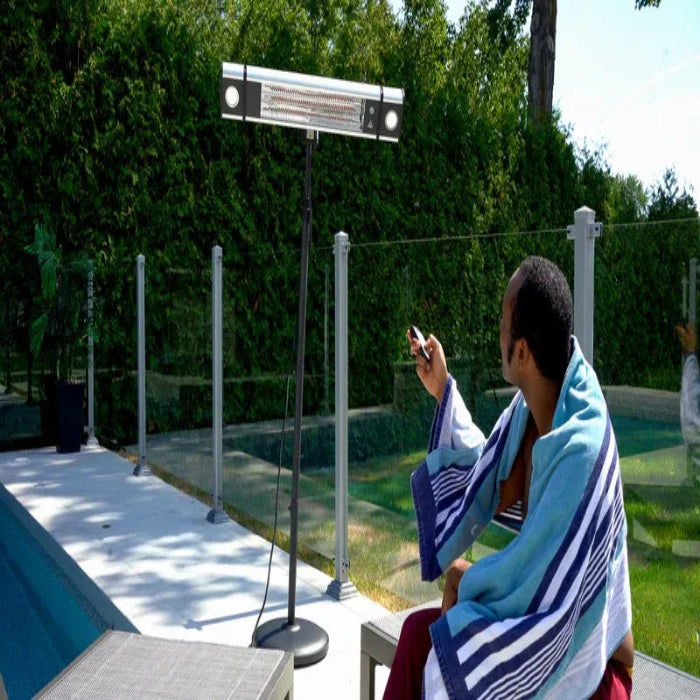 Person sitting on a chair with a blue towel draped over their shoulders, using a smartphone near a poolside heater.