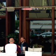 Two men sitting at an outdoor table with a reflective glass wall behind them.