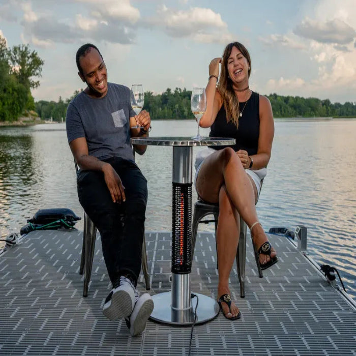 Two people sitting at a table by a lake, enjoying drinks.
