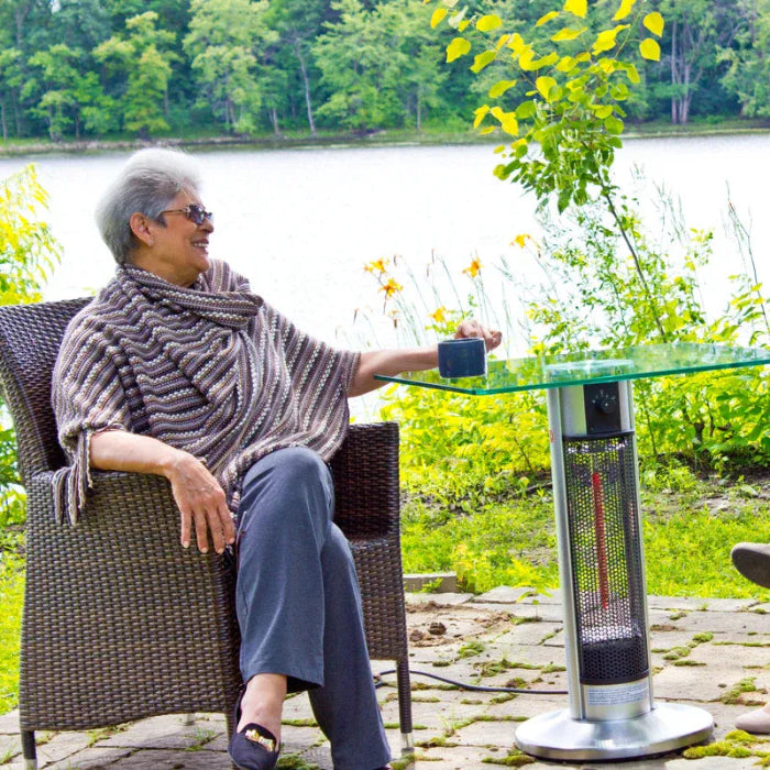 Person sitting outdoors by a lake, using a patio heater.