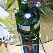 Green bottle with a solar panel on top, placed on a glass table outdoors.