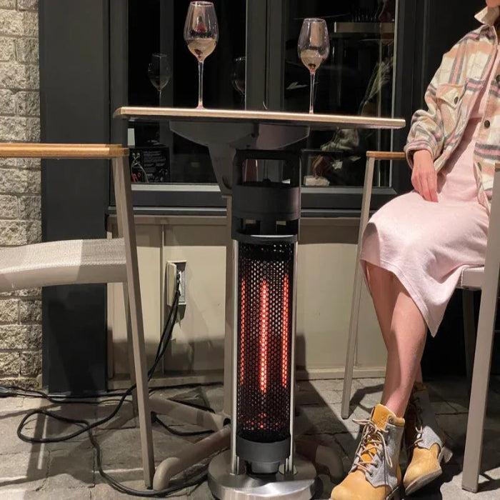 Outdoor patio heater with a person sitting nearby and a table with wine glasses.