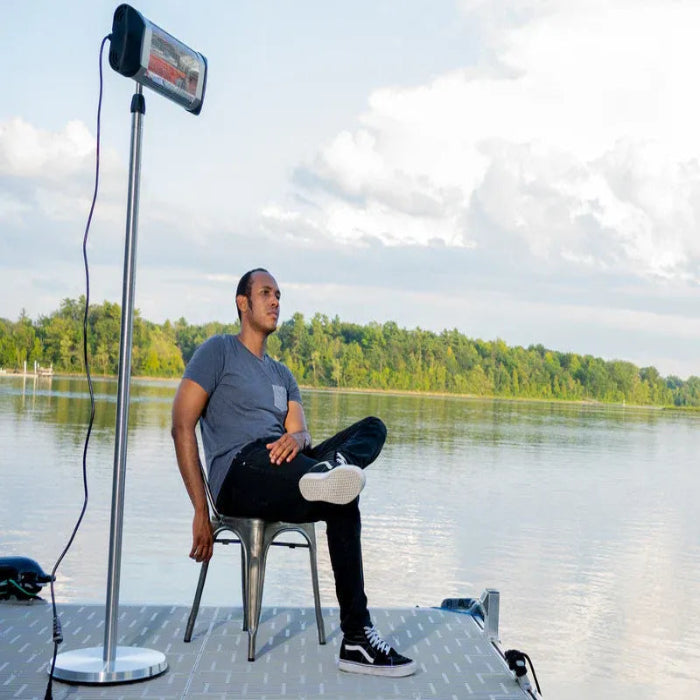 Person sitting on a chair by a lake with a large screen displaying an image.