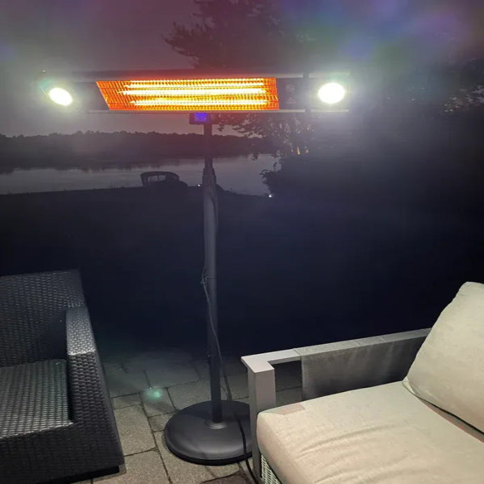 Outdoor patio heater on a patio with chairs by a body of water at night.
